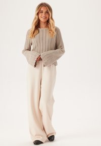 Maglione a coste color beige chiaro con maniche a campana e scollatura rotonda, abbinato a pantaloni larghi color crema e scarpe con tacco nere.