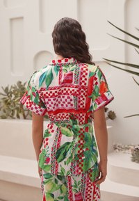 Többmintás ing, amely merész piros, zöld és rózsaszín mintákat tartalmaz levélmotívumokkal, rövid ujjakkal és derékrésznél szűkített részlettel.