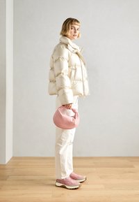 Krémová péřová bunda, růžová kabelka, bílé kalhoty a růžové tenisky s šedými akcenty. Bunda má vysoký límec a prošívanou texturu.