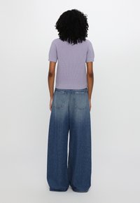 Top a maniche corte di colore lavanda a coste abbinato a jeans blu sbiaditi a gamba larga, dotati di tasche classiche e vestibilità comoda. Vista posteriore mostrata.