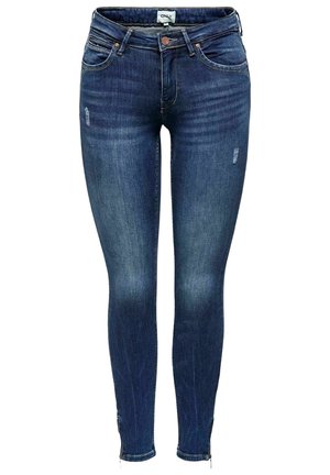 Jean skinny bleu foncé avec légère décoloration et zones usées, fermeture avant par bouton et fermeture éclair, et étiquette de marque sur la ceinture.