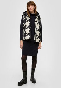 Kamizelka pikowana w czarno-białym wzorze w jodełkę; z kapturem; stylizowana na dopasowanej czarnej sukience; w połączeniu z czarnymi botkami za kostkę.