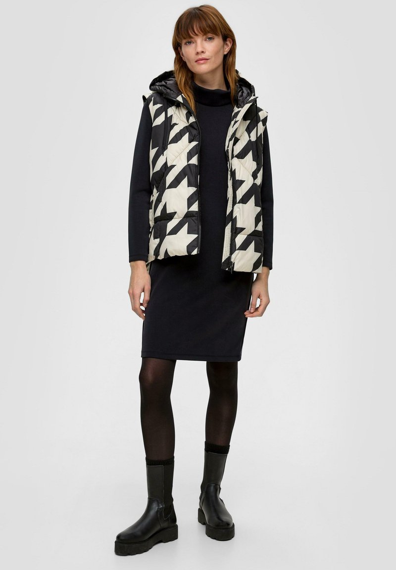 Kamizelka pikowana w czarno-białym wzorze w jodełkę; z kapturem; stylizowana na dopasowanej czarnej sukience; w połączeniu z czarnymi botkami za kostkę.