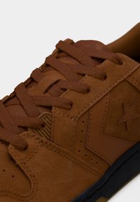 Καφέ σαμουάρ αθλητικό παπούτσι με κορδόνια, διακοσμημένο με αστέρι, με υφή στην επιφάνεια και αντίθετη μαύρη σόλα. Απλός σχεδιασμός με διάτρητες λεπτομέρειες.