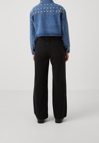 Sinine teksajakk, mille seljal on studidega kaunistus, koos mustade kõrge vöökoha laia säärega pükstega, millel on tagataskud.