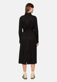 Schwarzes langärmeliges Kleid mit Kragen, tailliertem Gürtel und Rückenschlitz. Verfügt über sichtbare Nähte und einen leichten Stoff für eine entspannte Passform.