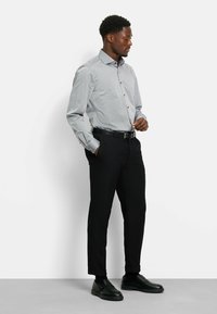 Grau kariertes Langarmhemd mit Button-Down-Kragen, kombiniert mit schlanken schwarzen Hosen und schwarzen Schuhen, die eine glatte Textur aufweisen.