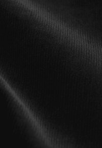 Tessuto nero con una superficie morbida e liscia decorata da sottili pattern a coste. Il materiale appare morbido e denso, enfatizzando la profondità.