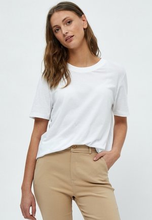 T-shirt en coton blanc à manches courtes et col rond, associé à un pantalon beige avec fermeture à bouton et poches latérales.