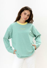 Groen en witte gestreepte sweatshirt met lange mouwen, een gele kraag en een logo op de borst. Zachte stof en een relaxte pasvorm.