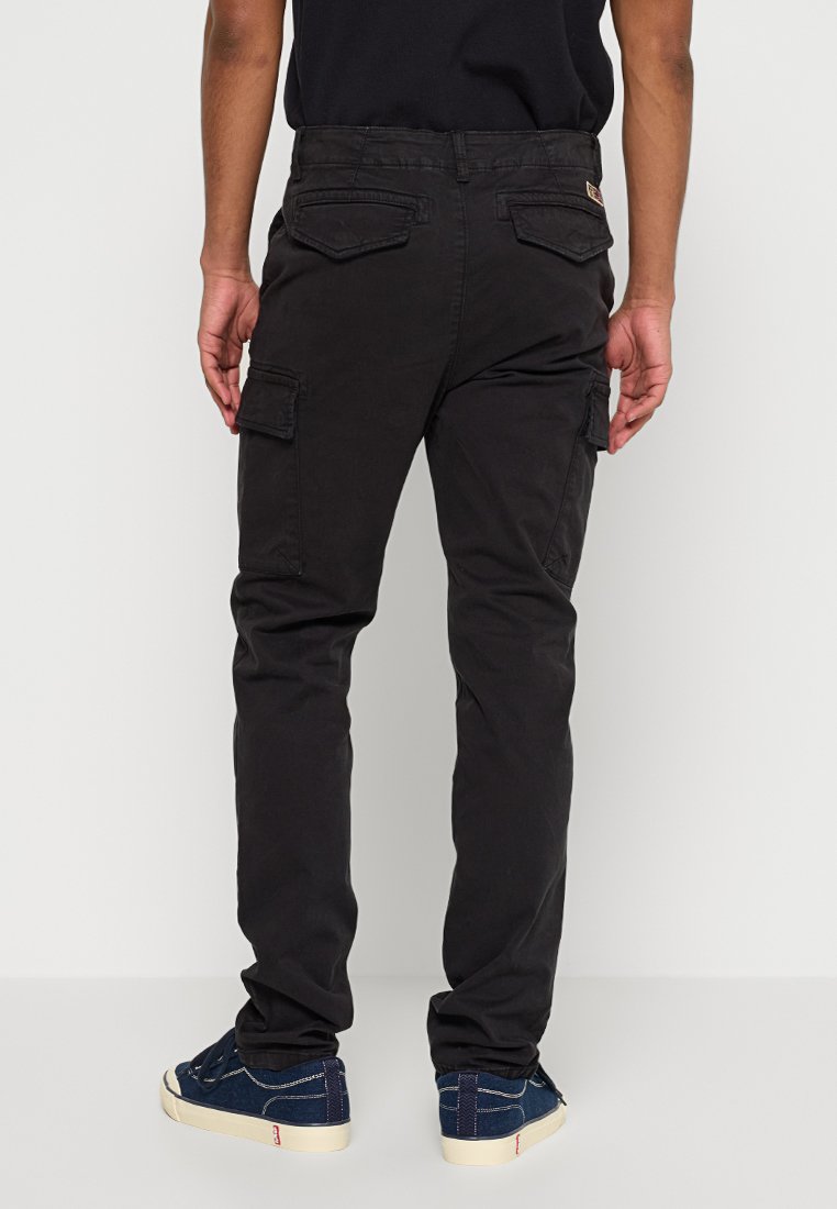 Pantalones cargo negros con bolsillos laterales y traseros, un corte recto y un material de algodón duradero, combinados con zapatillas deportivas azules.