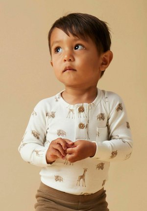 Långärmad cremefärgad skjorta med djurtryck, med träknappar, rund halsringning och en ficka; kombinerad med bruna byxor.