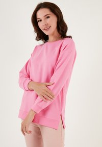 Felpa rosa a maniche lunghe con girocollo, fessure laterali all'orlo e polsini a costine. Materiale liscio ed elastico con una vestibilità comoda.
