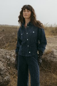 Navy textured jacket and pants set, featuring metallic buttons, pockets, and black leather gloves, set against a rocky landscape.