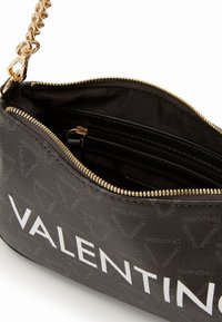 Černá kabelka se zlatým zipem a řetízkovým popruhem, s texturovaným povrchem a bílým logem "VALENTINO". Interiér obsahuje více kapes.