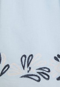 Ljusblått tyg med intrikat blommönster i marinblått och krämfärgat. Designen inkluderar slingor och kurvor, vilket skapar textur och djup.