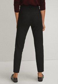 Pantalons noirs fuselés avec poches plates et texture lisse, dotés d'une taille mi-haute. Portés avec des mocassins noirs brillants.