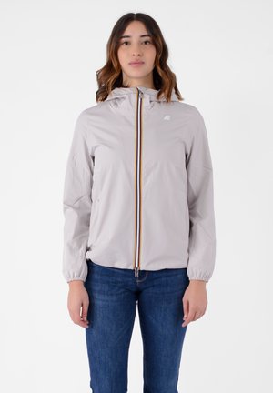 Giacca a vento grigia chiara con cappuccio, con una zip multicolore e polsini elastici, abbinata a jeans blu.