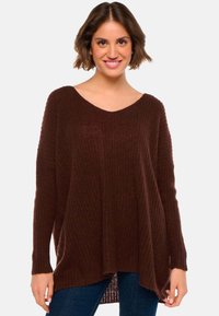 Pull en maille bordeaux avec un col en V, des manches longues, une coupe ample et une texture côtelée. Il dispose d'un ourlet asymétrique et d'un tissu doux et léger.