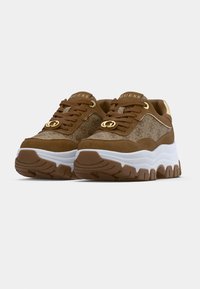Baskets à plateforme Guess marron et beige avec semelles blanches épaisses, lacets à l'avant et accents dorés du logo sur un fond uni.