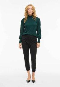 Maglione verde lavorato a maglia con colletto alto e maniche a sbuffo abbinato a pantaloni cropped neri aderenti e scarpe flat a punta.