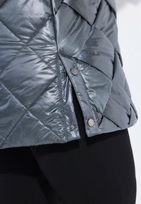 Gequilted donkergrijze pufferjack met een glanzende, metallic afwerking, drukknoopsluitingen en een diagonaal patroon, met een slank, modern ontwerp.