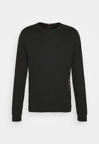 Black long-sleeve t-shirt made from cotton. Features a crew neck and a logo print along the left side. Smooth texture and regular fit.