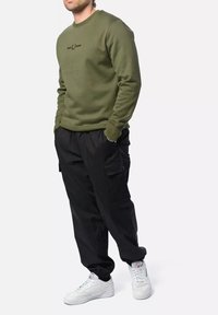 Sudadera verde oliva con cuello redondo y logo negro, combinada con pantalones cargo negros y zapatillas blancas. Ajuste casual, textura suave.