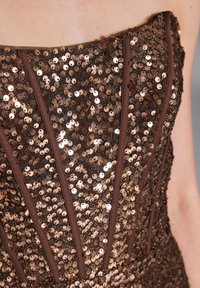 Vestido sin tirantes con un corsé de lentejuelas en tonos de bronce, con paneles de tela verticales que realzan su forma y textura reflectante.