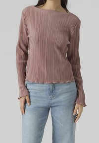 Dlouhý rukáv, řasený top v barvě pudrové růže, s lodičkovým výstřihem a třásněmi na lemu, spárovaný s světlými modrými džíny.