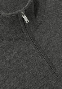 Pull en maille gris avec un col montant et un détail en zip argenté au niveau du cou, mettant en valeur un tissu texturé et un design épuré et minimaliste.