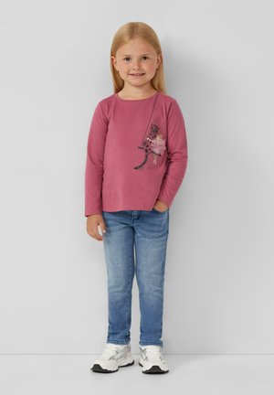 Roze blouse met lange mouwen met een speelse ontwerp en een versiering van een luipaard en bloemen, gecombineerd met lichtblauwe jeans en witte sneakers.