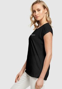 Sort kortærmet t-shirt med rund hals og let optrukne ærmer, lavet af blødt stof, med minimalistisk hvid tekst på forsiden.
