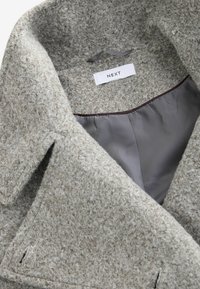 Beige wool blend coat with a soft, textured surface and a smooth gray lining. Features a notched collar and side pockets. Brand label visible.