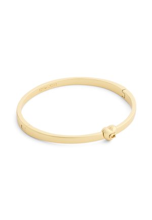 Bracelet jonc en métal doré Coach avec un fermoir en forme de cœur et un logo gravé sur la face intérieure.