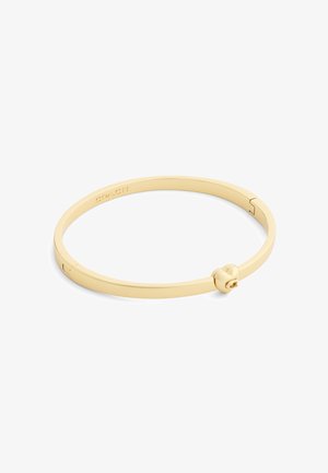 Gold-tone metal Coach bangle bracelet with a heart-shaped clasp and engraved logo on the inner side.