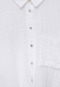 Chemise blanche à boutons avec un tissu texturé, dotée d'un col classique, d'une poche avant et de boutons irisés sur le plastron.