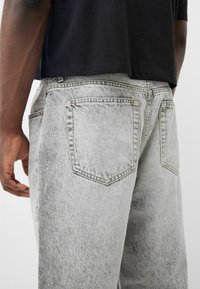 Ljusgrå denimjeans med en blekt textur, med två bakfickor och kontrasterande sytråd. Bärs med en svart t-shirt med kort ärm.