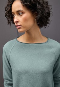 Felpa teal con un tessuto morbido e strutturato e maniche raglan. Presenta un collo arrotondato e sottili dettagli di cucitura.