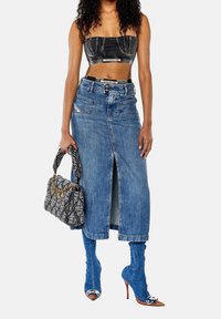 Zwarte denim cropped top, lange blauwe denimrok met een voorste split, blauwe over-de-knie laarzen, en een grijze gewatteerde handtas met gouden kettingaccenten.