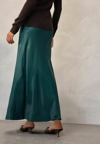 Teal satiinimaksihame, jossa on virtaava leikkaus, täydentää tiukka ruskea ribbipaita ja kuvioidut avokärkiset korkokengät.