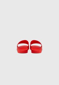 Sandale roșii din cauciuc cu design cu curea deschisă, tălpi plate și o textură netedă. Formă simplă, minimalistă, fără modele sau accente vizibile.