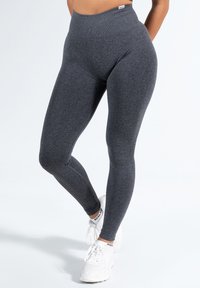 Legginsy o wysokim stanie w ciemnoszarym kolorze, z gładką fakturą i dopasowanym krojem, w zestawie z białymi butami sportowymi.