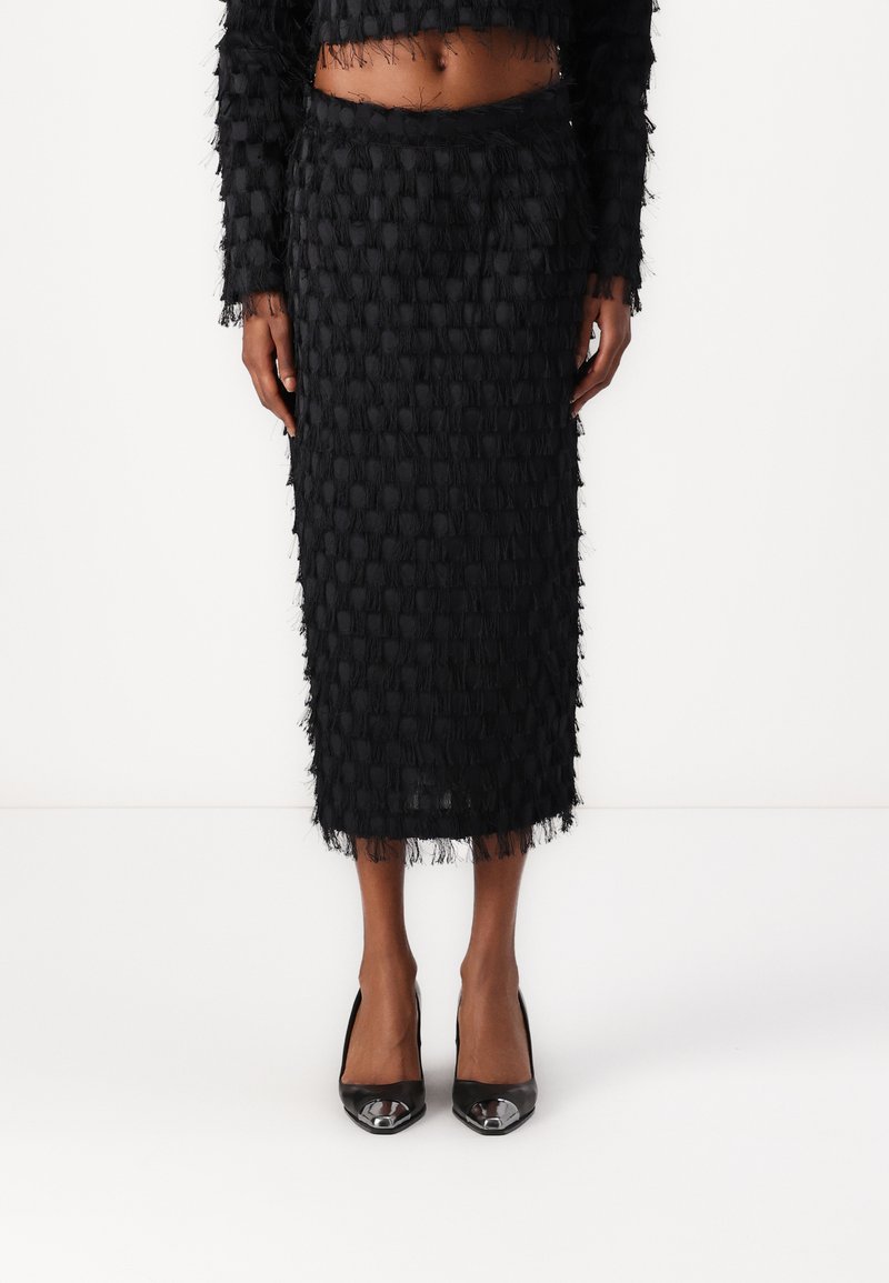 Black textured two-piece outfit featuring a cropped top with fringe details and a midi skirt with a similar pattern. Paired with shiny black heels.