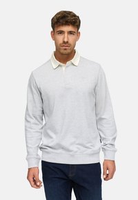 Lys grå langærmet polo skjorte med en kridhvid krave, ribbede manchetter og et diskret logo på brystet. Båret med mørkeblå jeans.