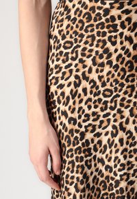 Venstre hånd hviler ved siden af leopardtrykstof med beige, sort og brune pletter på lys baggrund.