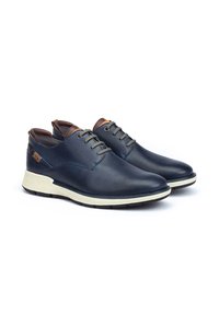Chaussures en cuir bleu marine avec une texture perforée, dotées de lacets gris, d'accents marron et d'une semelle en caoutchouc de couleur claire.