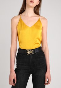 Yellow satin tank top with a deep V-neck. Paired with high-waisted black jeans and a black belt featuring a gold bee buckle accent.