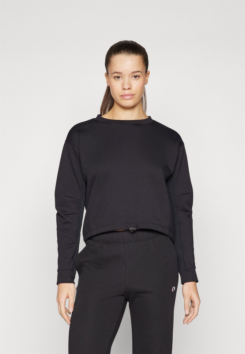 Black cropped sweatshirt with long sleeves, round neckline, textured cotton blend, adjustable drawstring at the hem, paired with black sweatpants.