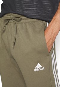 adidas Sportswear ESSENTIALS TAPERED CUFF 3-STRIPES  - Treniņtērpa apakšdaļas - olive strata